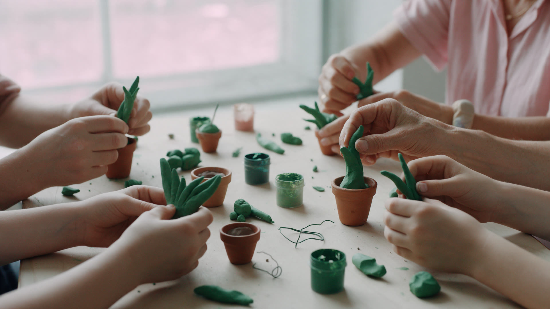 A workshop table where several people shape their own small clay plants in tiny terracotta pots.